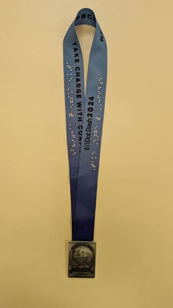 A 6 Dot Dash medal lays on a table. The medal says, “Change the World” and “Confidence.