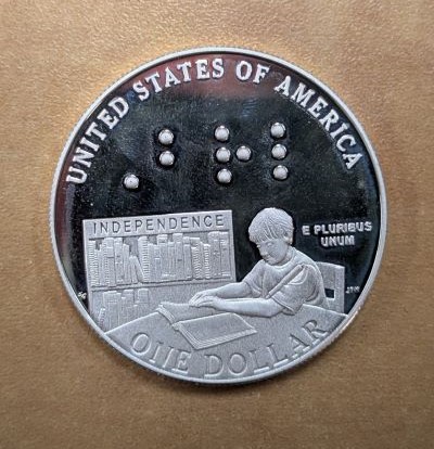 One side of the Braille silver dollar coin