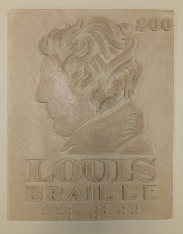 A profile of Louis Braille on a tactile plaque. Underneath, the raised print text reads “Louis Braille”